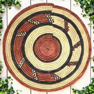Woven raffia rust, black and natural Burkina platter with a hook pattern, on white timber with greenery