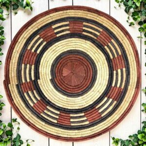 Woven raffia rust, black and natural Burkina platter with a band pattern, on white timber with greenery