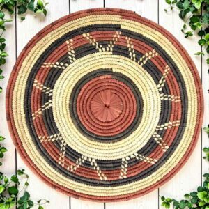 Woven raffia rust, black and natural Burkina platter with a zigzag pattern, on white timber with greenery
