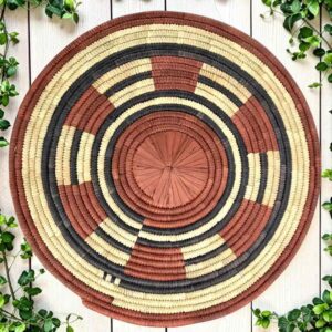 Woven raffia rust, black and natural Burkina platter with a segment pattern, on white timber with greenery