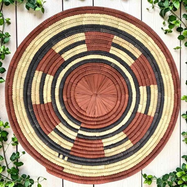 Woven raffia rust, black and natural Burkina platter with a segment pattern, on white timber with greenery