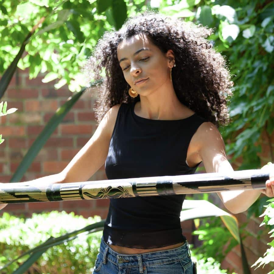 a woman playing a bamboo rainstick shaker outdoors