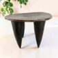 Dark hardwood Senufo stool with an oval seat and four tapered legs, styled beside a plant