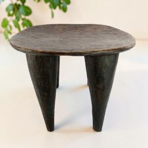 Dark hardwood Senufo stool with a rounded square seat, styled beside a plant
