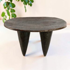 Low dark hardwood Senufo stool with a wide, elongated seat, styled beside a plant