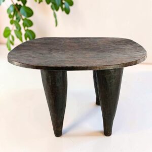 Dark hardwood Senufo stool with a broad, dished seat, styled beside a plant
