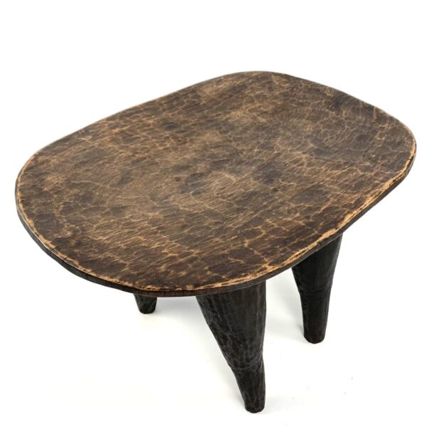 bashiri-senufo-stool-ivorycoast-071-fable-west-african-stool-wooden-3 Angled view of the carved seat of the Senufo stool with a lighter worn seat and dark tapered legs