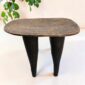 Senufo stool with a lighter worn seat and dark tapered legs, styled beside a plant
