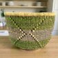 Large Uba Bolga basket in green, purple and natural straw with woven geometric pattern, styled on a timber table
