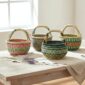 Four vegan small round Bolga baskets on a timber table, each with a different woven colour pattern including pink and green, charcoal, teal and yellow, and green and coral