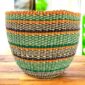 Handwoven planter basket in green, orange and black diagonal stripe pattern on a timber surface