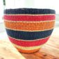 Woven planter basket in bold red, orange and black horizontal stripes on a timber table