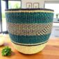 Teal and black woven planter basket with natural straw base on a timber bench