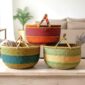 XL round Bolga baskets handwoven in Ghana, shown in three colour variations including warm red and orange, teal and mustard, and natural green stripe, with leather handles.