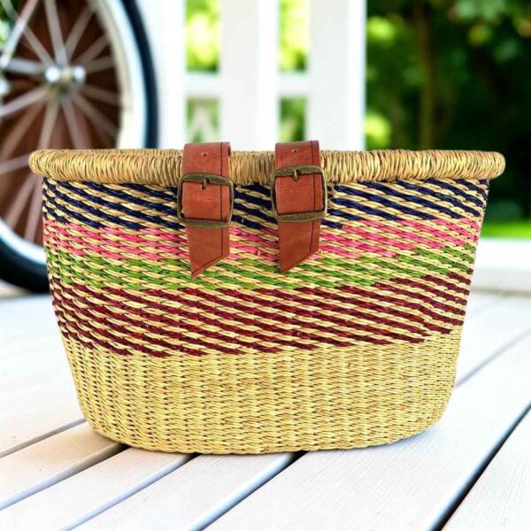 Natural Bolga bike basket with diagonal navy, pink, green, and maroon stripes, leather straps and buckles