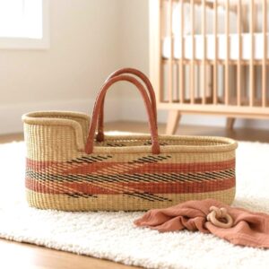 Moses basket with a rust band and black zigzag lines on a nursery rug beside a folded blanket