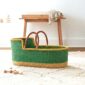 Green Moses baby basket with a yellow rim on a rug in a nursery