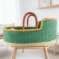 Moses basket with a solid green body, yellow rim, natural base and leather-wrapped handles