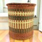 a woven laundry basket in natural, brown, and olive colours, with a lid.