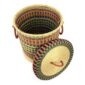 The closed laundry basket with its lid off, showing multicoloured orange, blue and yellow stripes above a natural base, with a woven lid and leather ring handles