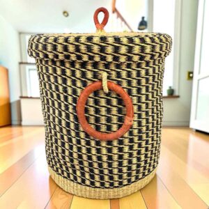 Closed laundry basket with a black and natural check, a woven lid and leather ring handles