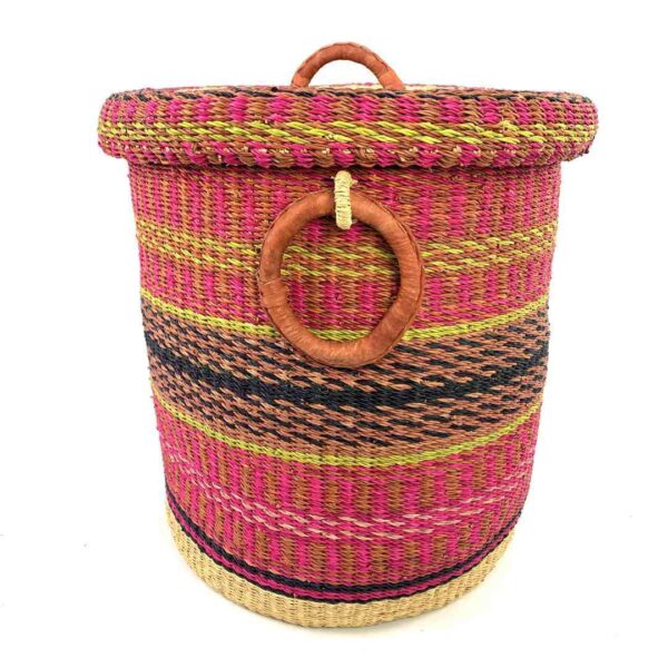 closed-laundry-basket-0308-tinsel-pink-african-bashiri-3 Front view of the closed laundry basket with bright pink with gold and black bands, a patterned woven lid and leather ring handles on a white background