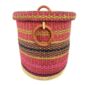 Front view of the closed laundry basket with bright pink with gold and black bands, a patterned woven lid and leather ring handles on a white background