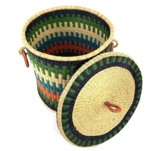 The closed laundry basket with its lid off, showing green, teal and orange stripes, a woven lid and leather ring handles