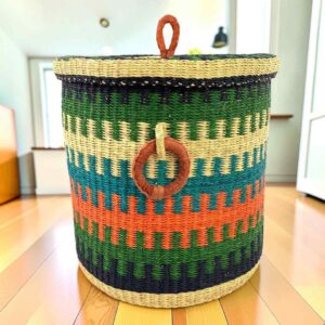 Closed laundry basket with green, teal and orange stripes, a woven lid and leather ring handles