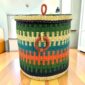 Closed laundry basket with green, teal and orange stripes, a woven lid and leather ring handles