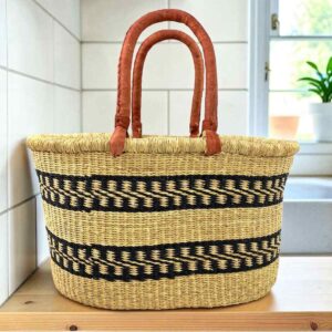 Extra large oval Bolga basket with two black stepped bands on natural straw and leather handles, on a wooden kitchen bench