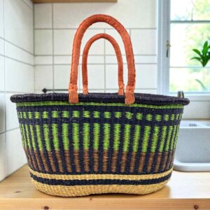 Extra large oval Bolga basket with lime green vertical stripes over navy, with a navy rim and leather handles, on a wooden kitchen bench