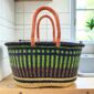 Extra large oval Bolga basket with lime green vertical stripes over navy, with a navy rim and leather handles, on a wooden kitchen bench