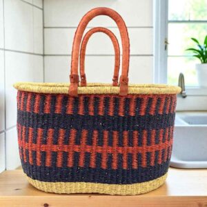 Extra large oval Bolga basket with rust orange and navy bands and leather handles, on a wooden kitchen bench