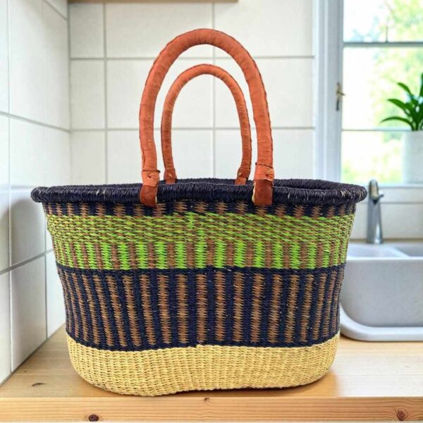 extra-large-oval-013-grassland-green-navy-basket-woven-bashiri-main Extra large oval Bolga basket with a lime green band between a navy rim and navy lower body and leather handles, on a wooden kitchen bench