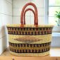 Extra large oval Bolga basket with black and mustard bands with a central diamond motif and leather handles, on a wooden kitchen bench