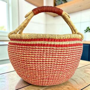 XL round Bolga basket with fine red and natural stripes and a leather-wrapped handle, on a wooden table