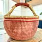 XL round Bolga basket with fine red and natural stripes and a leather-wrapped handle, on a wooden table