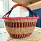 XL round Bolga basket with upright orange and black stripes, a pink rim and a leather-wrapped handle, on a wooden table