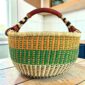 XL round Bolga basket with orange and green checks over a natural base and a striped leather handle, on a wooden table