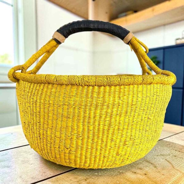 Solid yellow XL round Bolga basket with a black leather-wrapped handle, on a wooden table