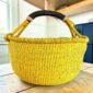 Solid yellow XL round Bolga basket with a black leather-wrapped handle, on a wooden table