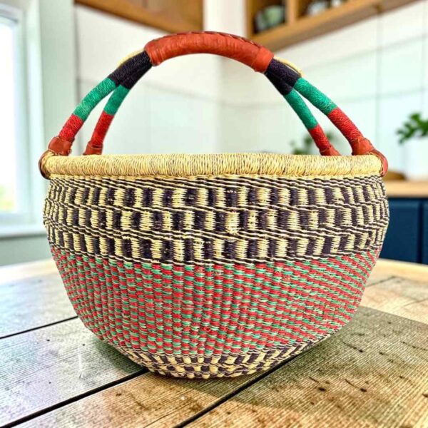 XL round Bolga basket with black checked bands over a red and green speckled weave and a striped leather handle, on a wooden table