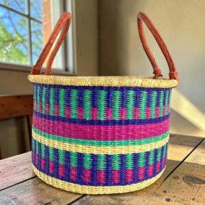Medium hamper basket with jewel-toned stepped stripes and leather handles, on a wood table