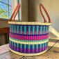 Medium hamper basket with jewel-toned stepped stripes and leather handles, on a wood table