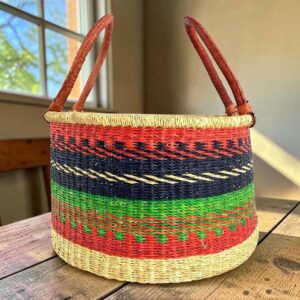 Hamper basket in warm and dark-toned stripes with leather handles, on a wood table