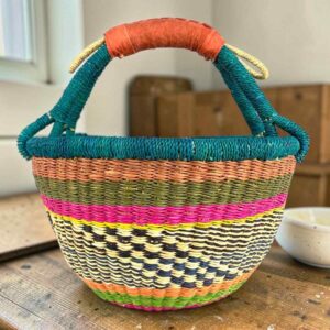 Medium round Bolga basket with a teal-wrapped rim and handle over terracotta, olive and magenta bands with a black-and-cream diamond weave, leather handles