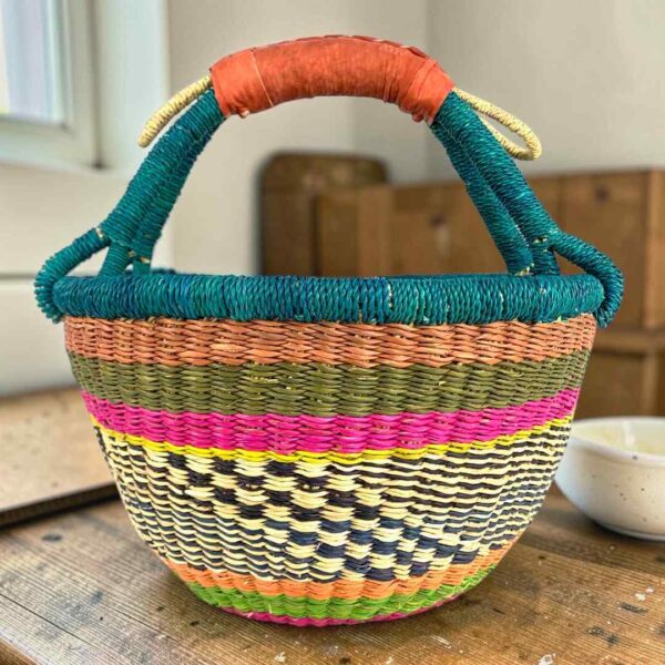 Medium round Bolga basket with a teal-wrapped rim and handle over terracotta, olive and magenta bands with a black-and-cream diamond weave, leather handles