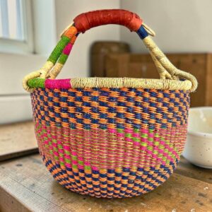 Medium round Bolga basket with a navy, orange, magenta and green checkerboard weave, leather handles