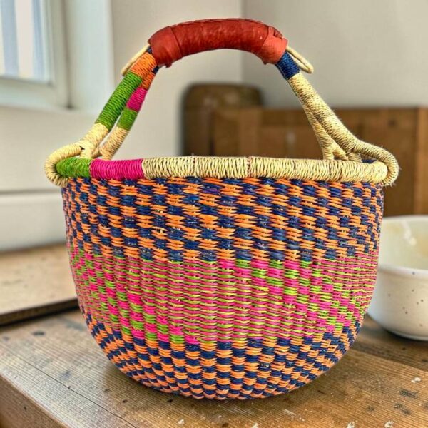 Medium round Bolga basket with a navy, orange, magenta and green checkerboard weave, leather handles
